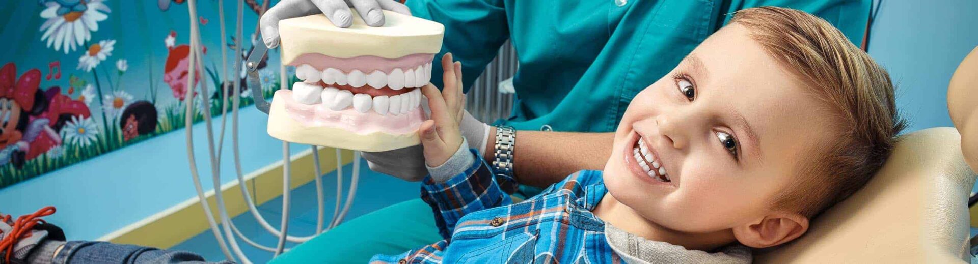 Yeşil önlüklü hekim çocuğa büyük diş modeli üzerinde fırçalamayı gösteriyor